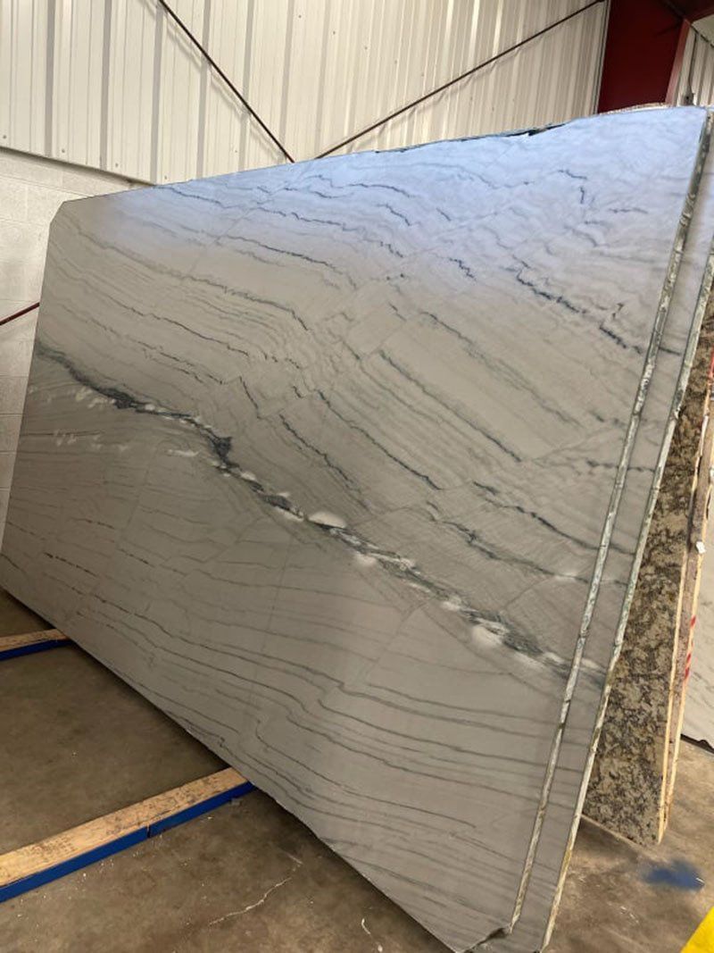 White and gray stone slab with wavy patterns and dark veining, possibly marble, stacked in a warehouse.