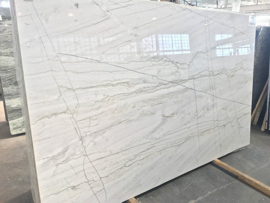 Large white marble slab with gray and gold veining, displayed in a showroom.