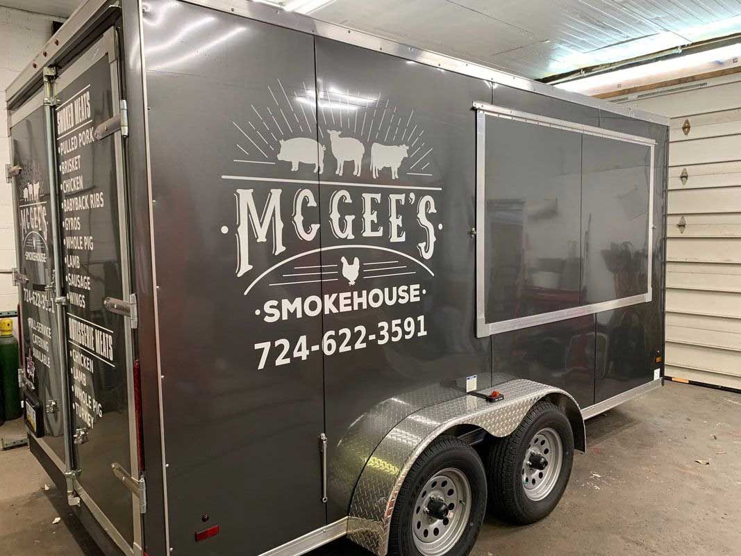 Gray McGee's Smokehouse food trailer with logo, menu, and phone number (724-622-3591); parked indoors.