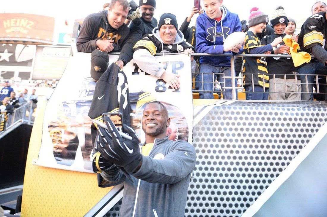 Steelers player taking a selfie with fans at a parade. Fans wear black and gold, cheering.