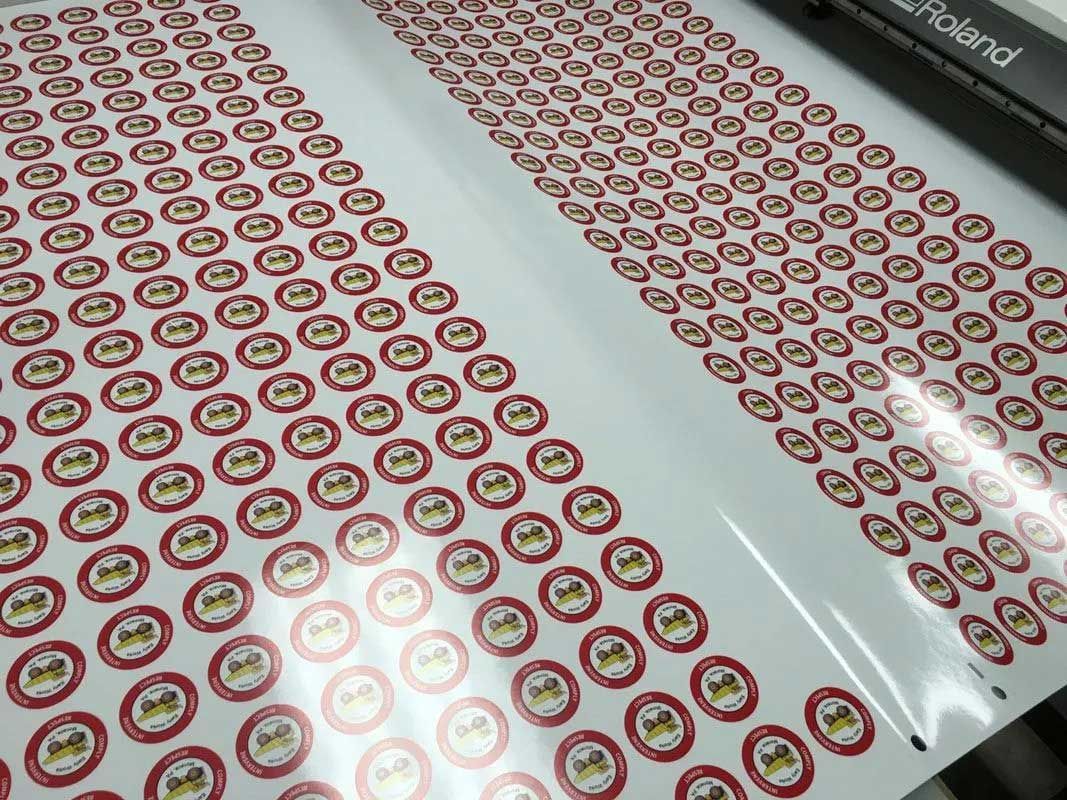 Roll of stickers with a red and gold circular design being printed by a Roland machine.