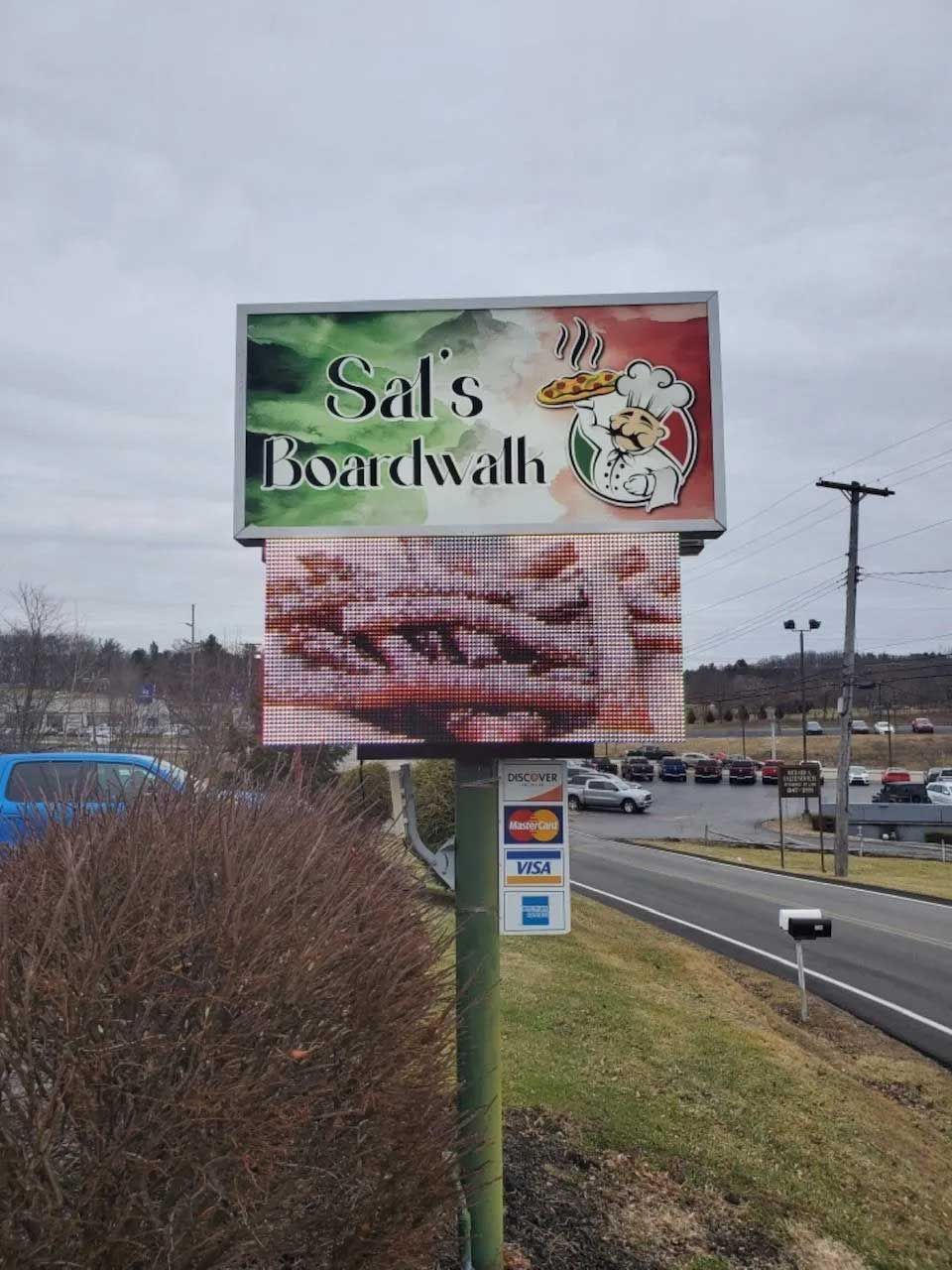 Sign for Sal's Boardwalk restaurant, with Italian flag colors and a faded pizza graphic. Roadside location.