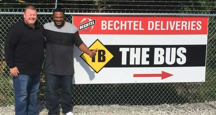 Two men pose in front of a sign: