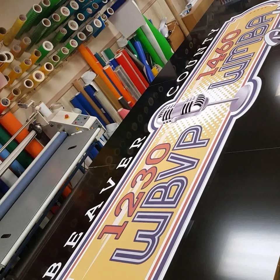 A sign for 1230 WBVP Beaver County radio station in brown, orange, and white with a microphone graphic.