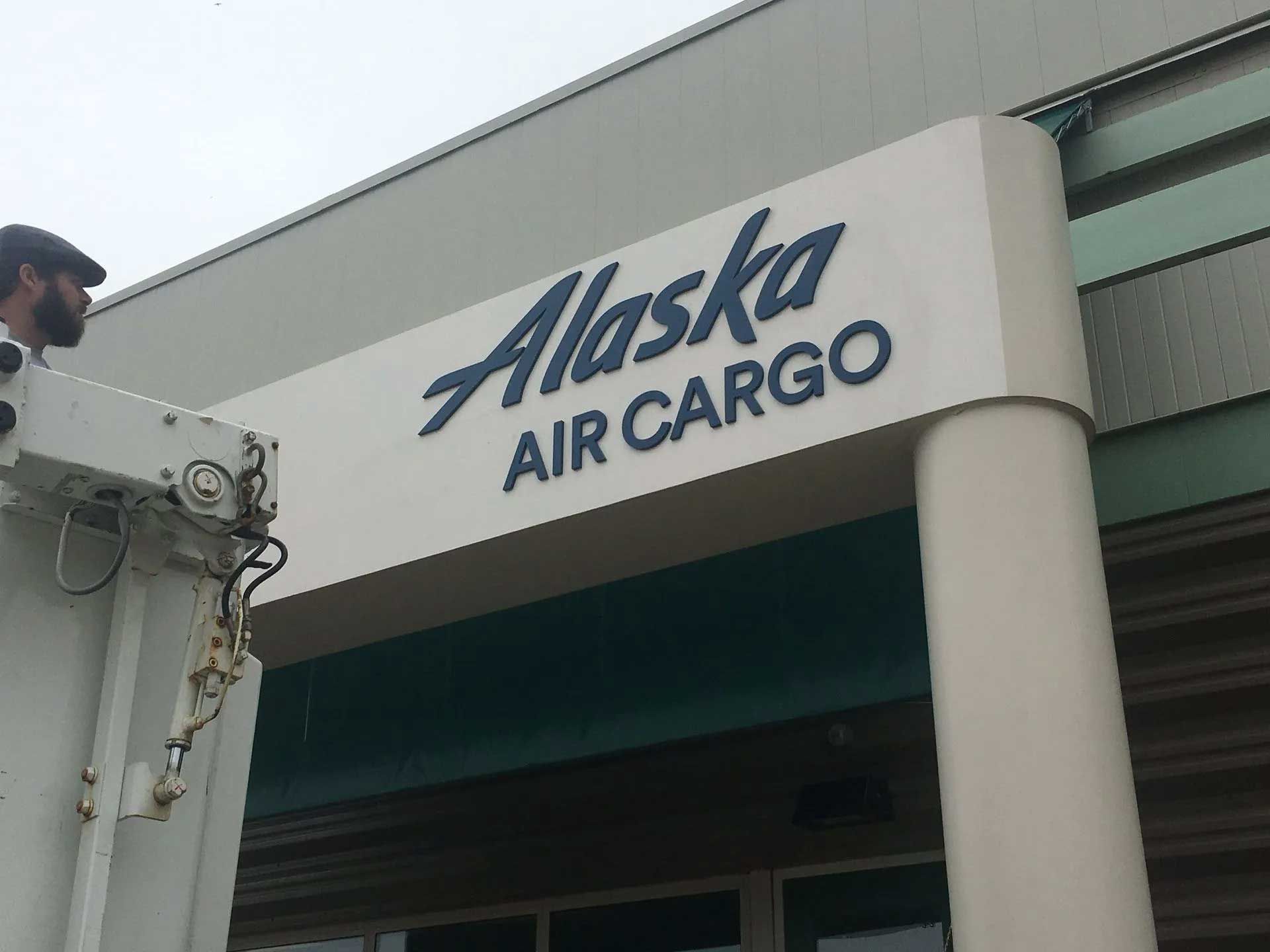 Alaska Air Cargo sign on building facade; worker in lift.