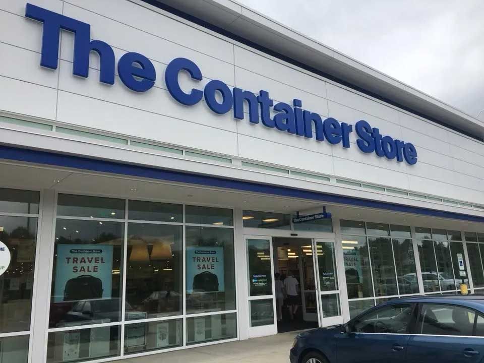 Exterior of The Container Store with blue signage and a blue car parked in front.