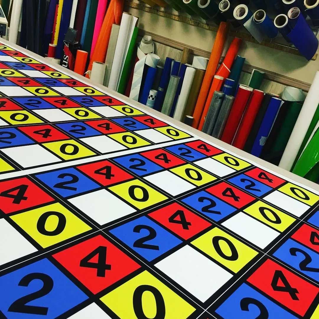 Checkerboard design with numbers 0, 2, and 4 in red, blue, and yellow squares on a table with rolls of material in the background.