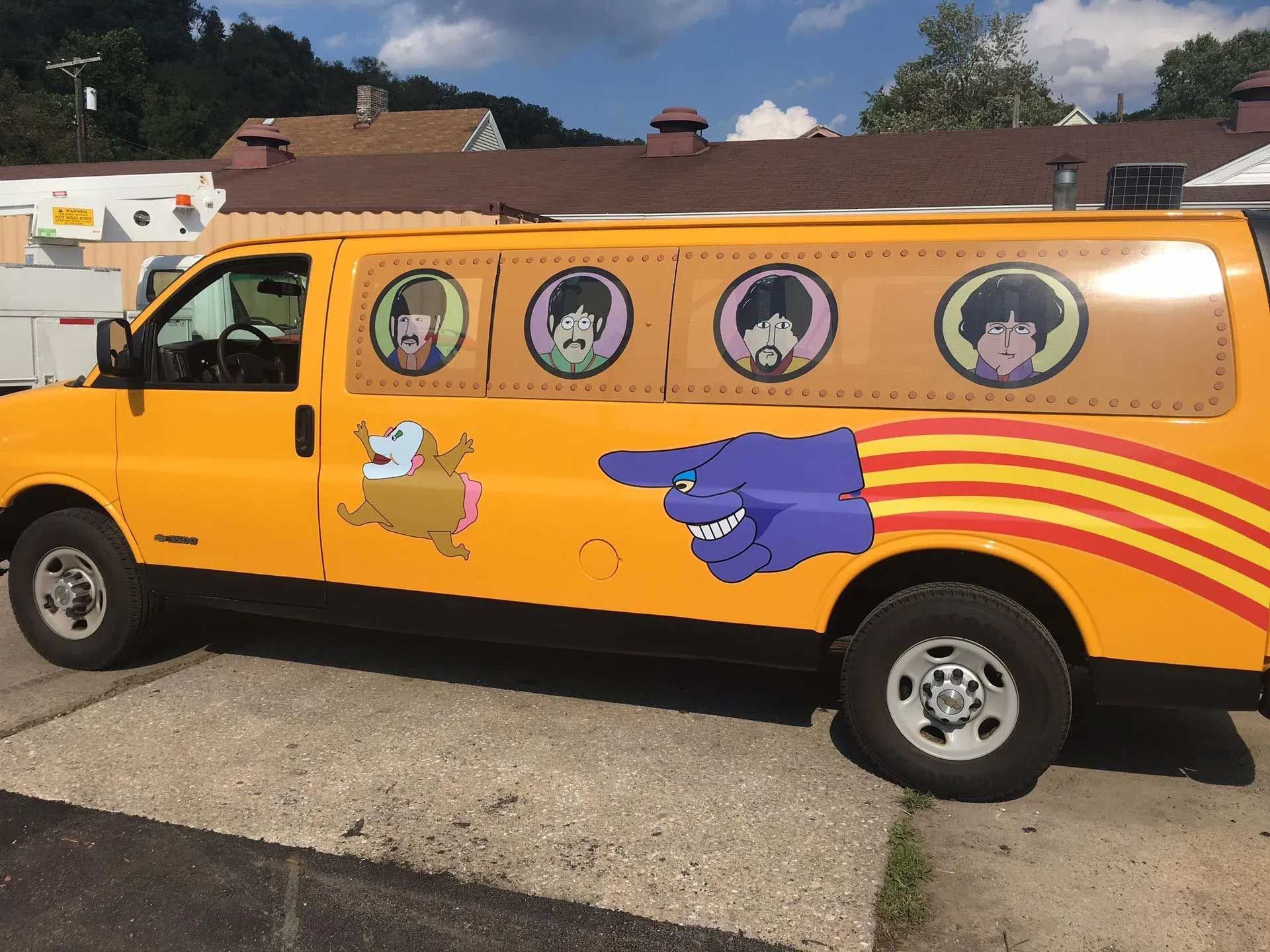 Yellow van with cartoon characters on the side. Beatles-esque heads in windows.