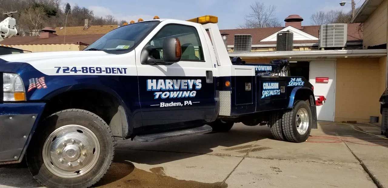 Blue and white Harvey's Towing truck parked outside a building, with the tow arm visible.