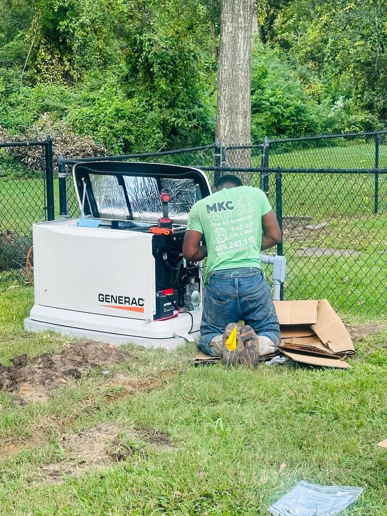 Man in green shirt installing a Generac generator in a grassy yard, near a tree.