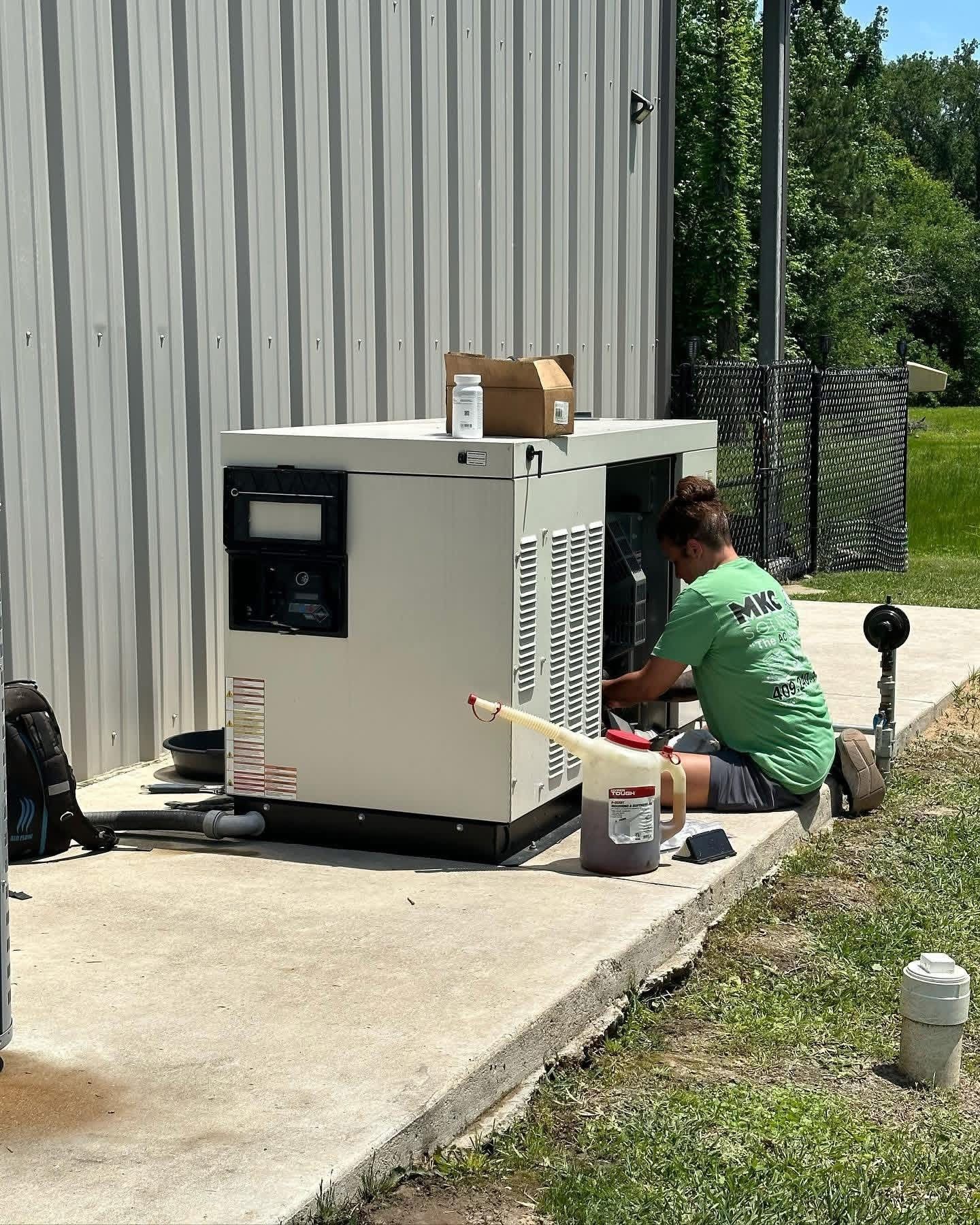 Technician in a green shirt performs maintenance on a beige backup generator sitting on a concrete pad outdoors.
