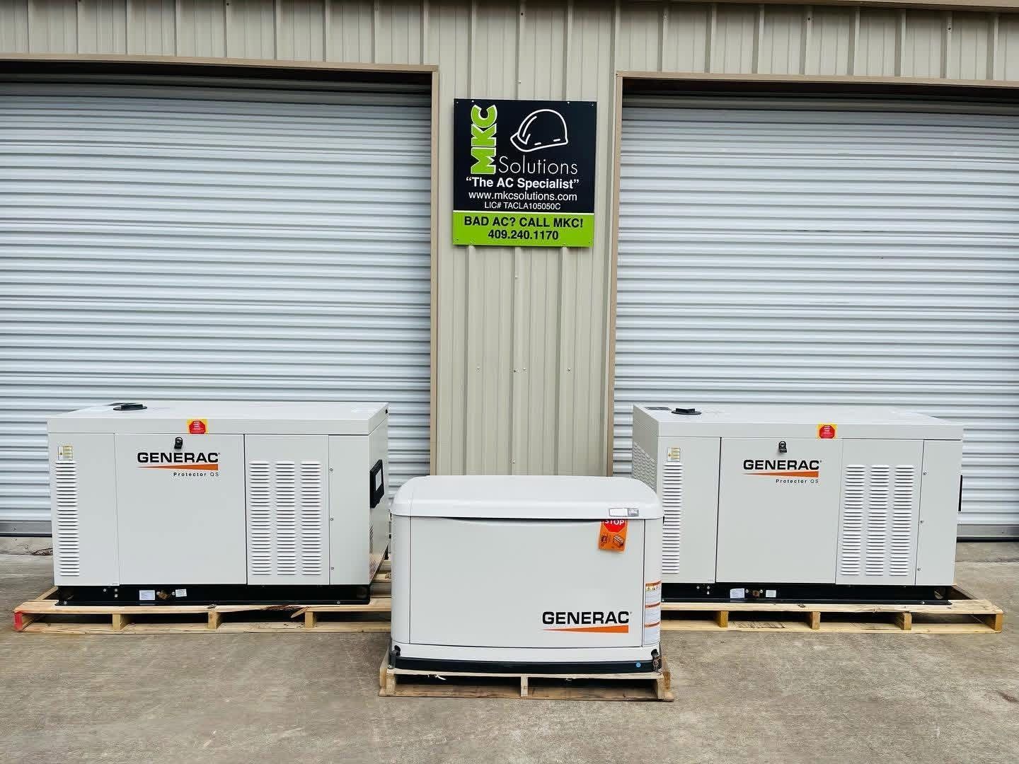 Three white Generac standby generators on wooden pallets in front of a building with roll-up metal doors.