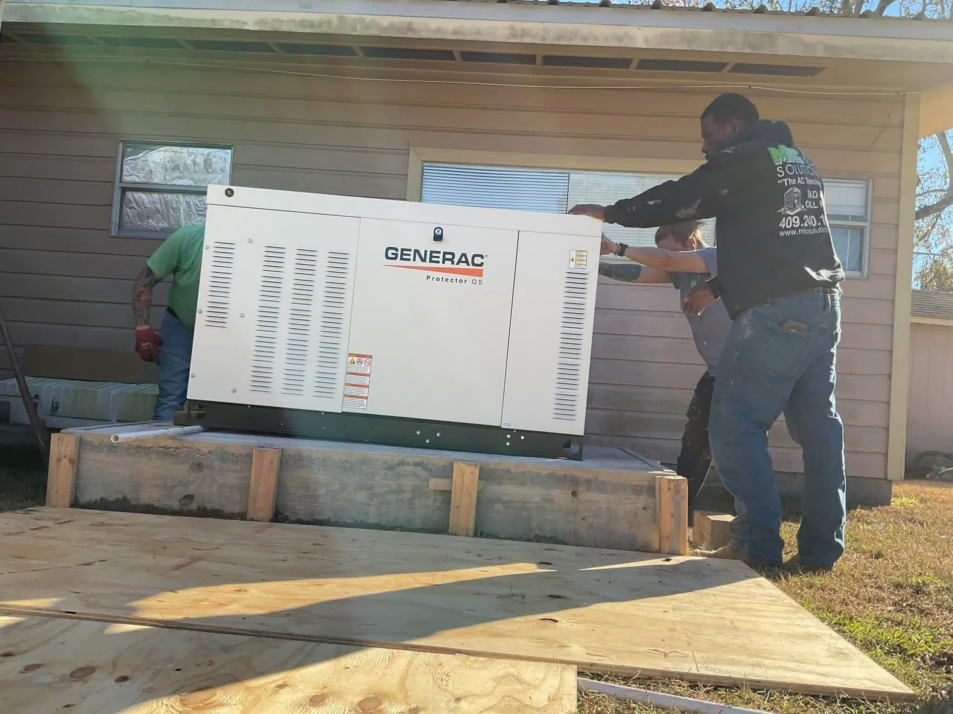 Two workers maneuvering a large white Generac generator onto a concrete pad outside a house.