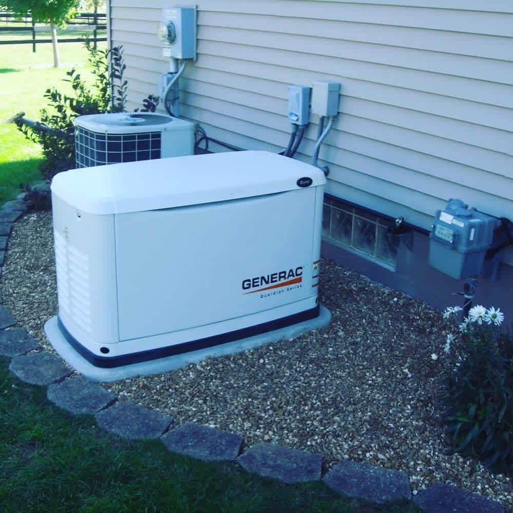 A white Generac backup generator installed on a gravel bed next to the exterior wall of a house.