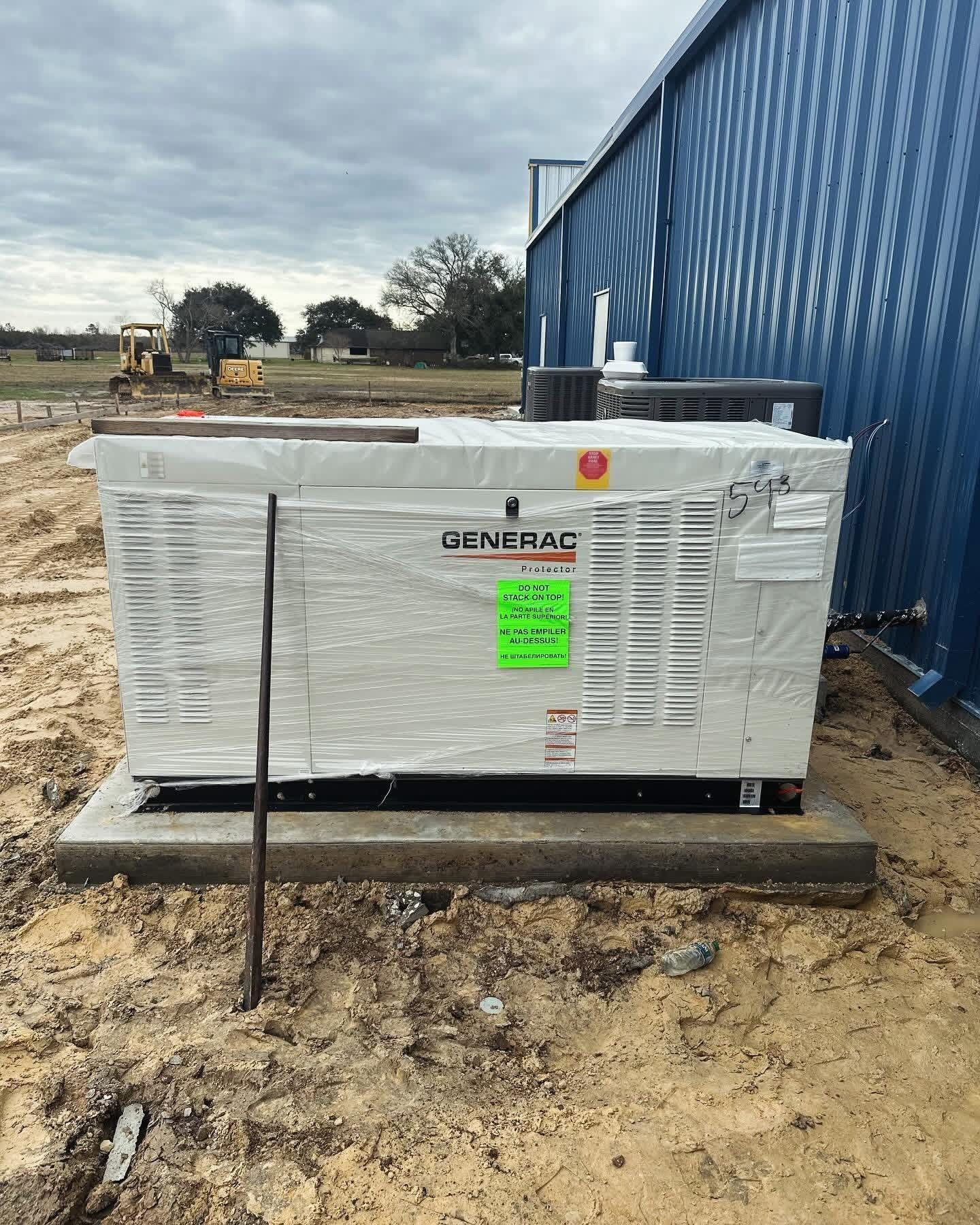 A wrapped Generac backup generator on a concrete pad next to a blue metal building at a construction site.