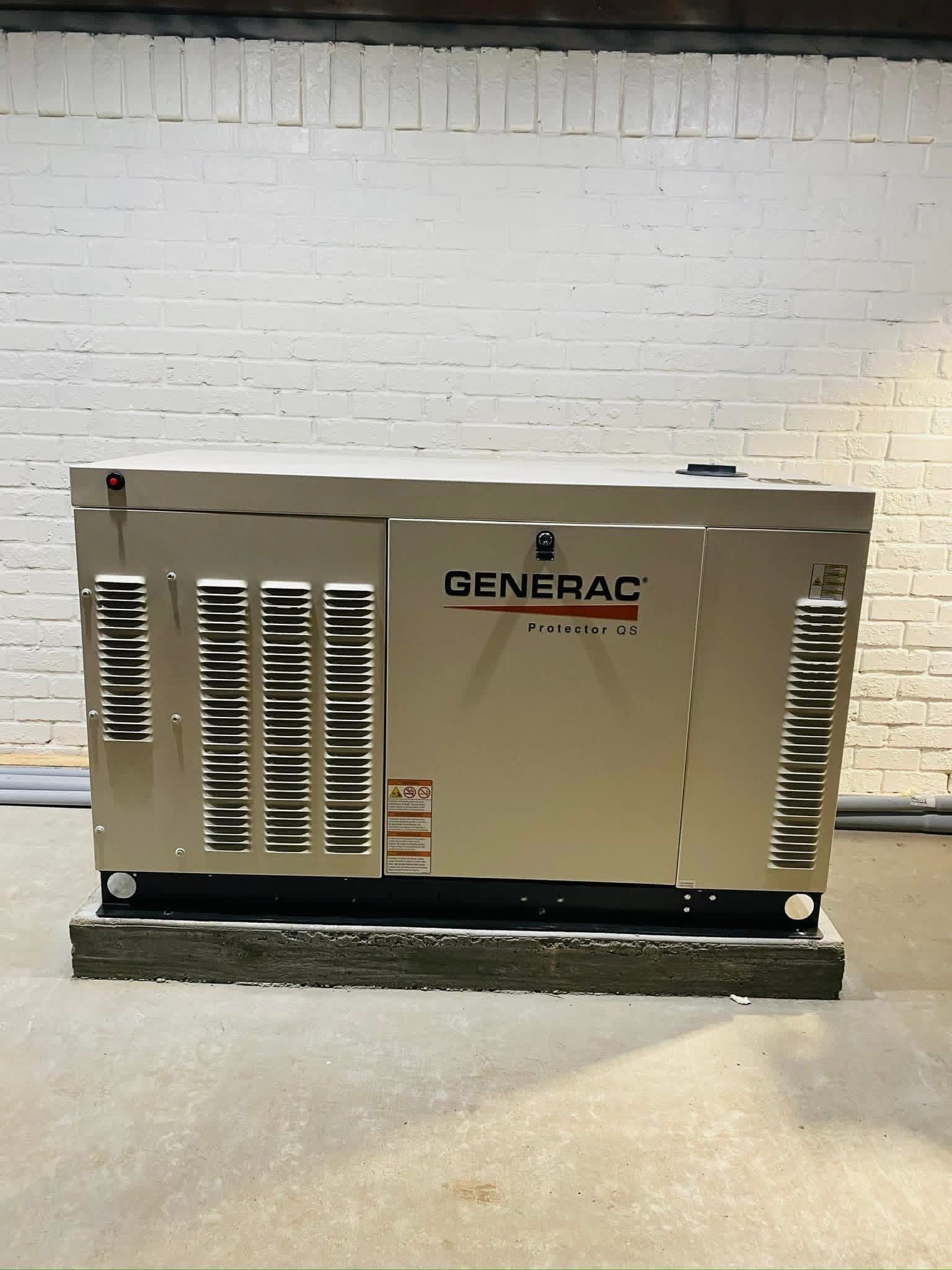 A beige Generac standby generator sits on a concrete base against a white brick wall.