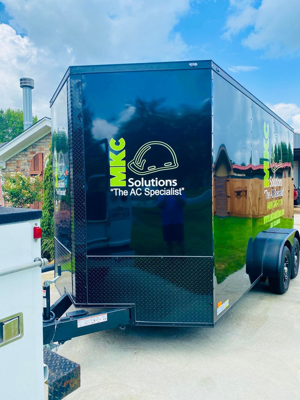 A black trailer is parked in a driveway next to a house.