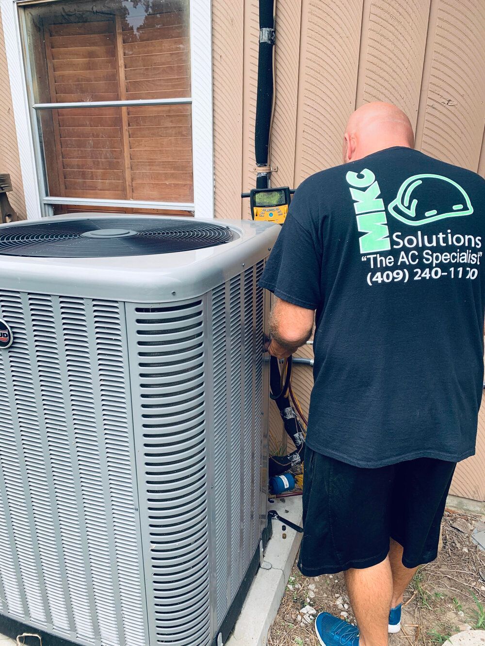 A man is working on an air conditioner outside of a house.