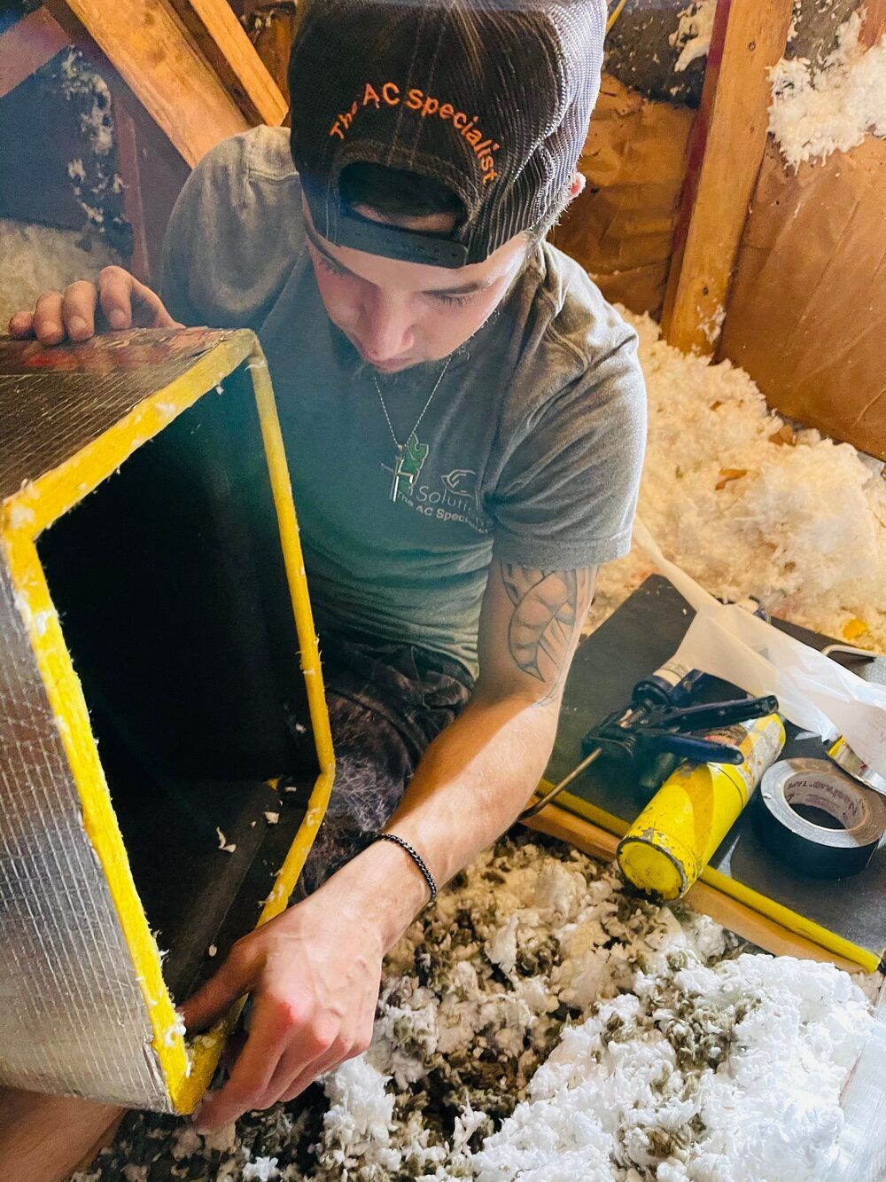 A man wearing a hat is working on a box in an attic.