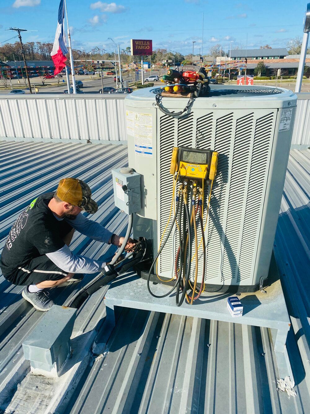 A man is working on an air conditioner on the roof of a building.