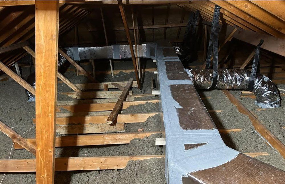 An attic with wooden beams and ducts hanging from the ceiling.