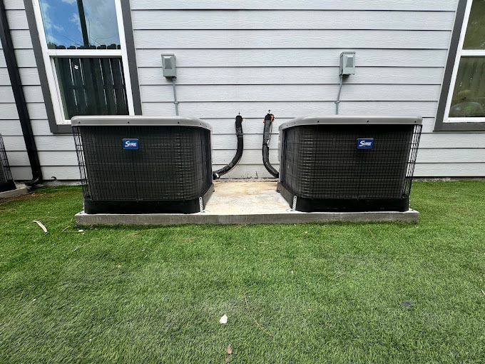 Two air conditioners are sitting next to each other on the side of a house.
