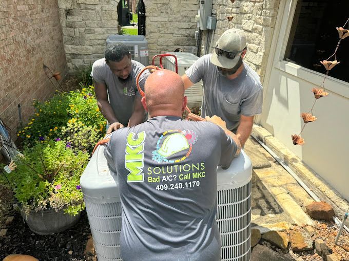 A group of men are working on an air conditioner outside of a house.