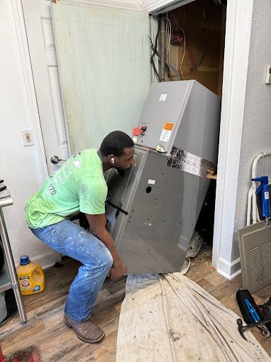 A man is squatting down next to a refrigerator in a room.