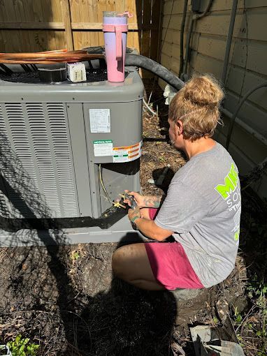 A woman is kneeling down in front of an air conditioner.