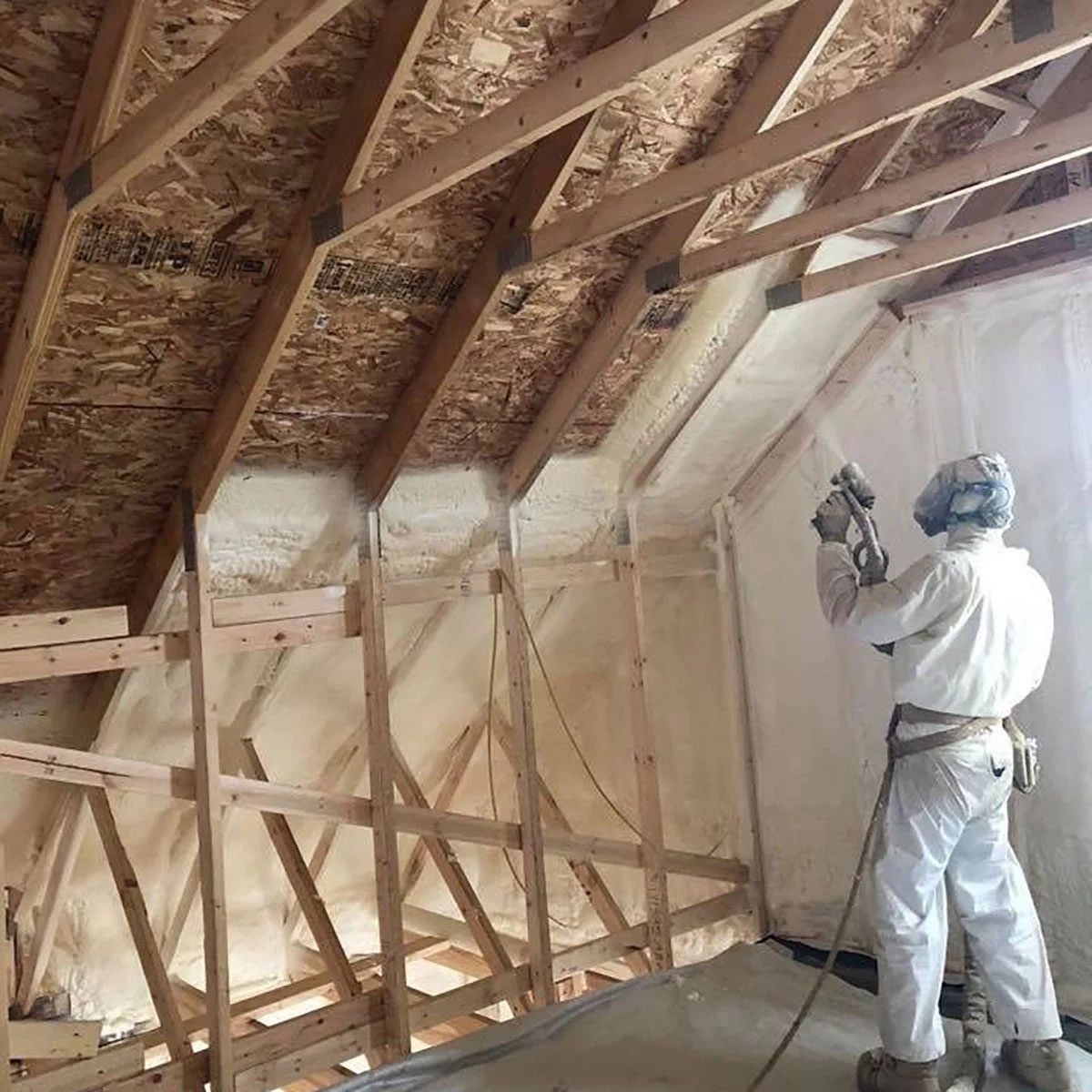 A man is spraying insulation on the roof of a house.