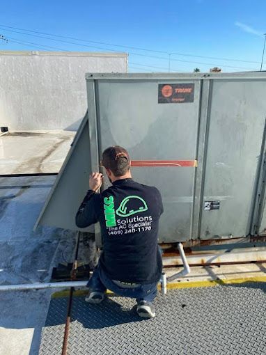 A man is kneeling down next to a large metal box on top of a roof.