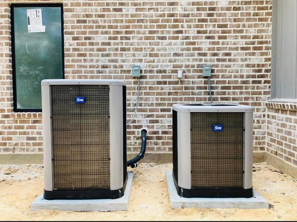 Two air conditioners are sitting next to each other in front of a brick building.