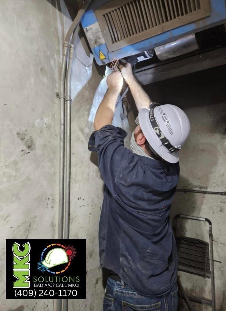 Man in hard hat working on machinery near a wall; indoor setting.