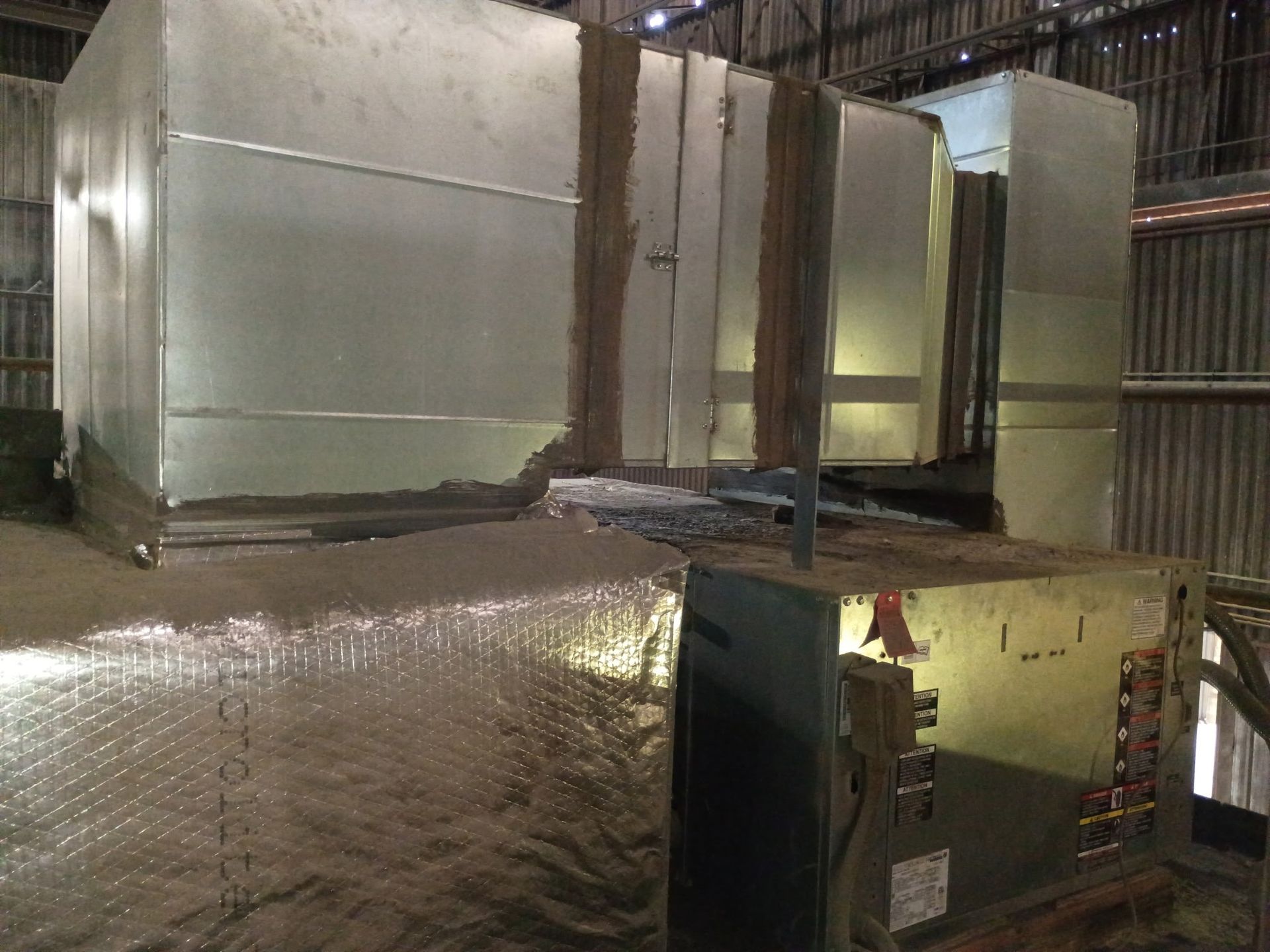 Large, silver HVAC ductwork with insulation in a warehouse setting.
