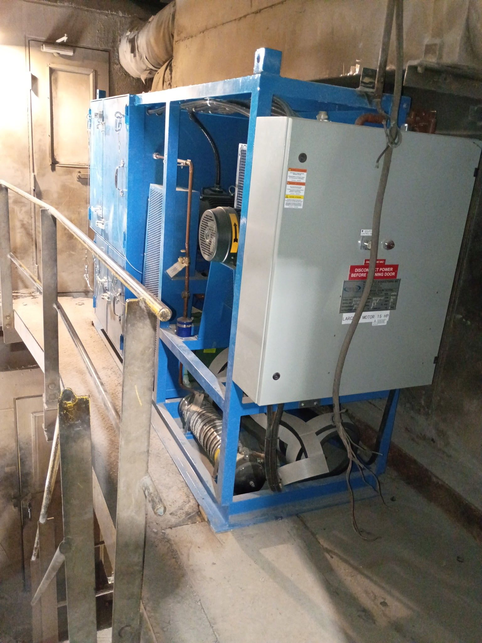 Blue industrial machine with gray electrical panel on a metal walkway.
