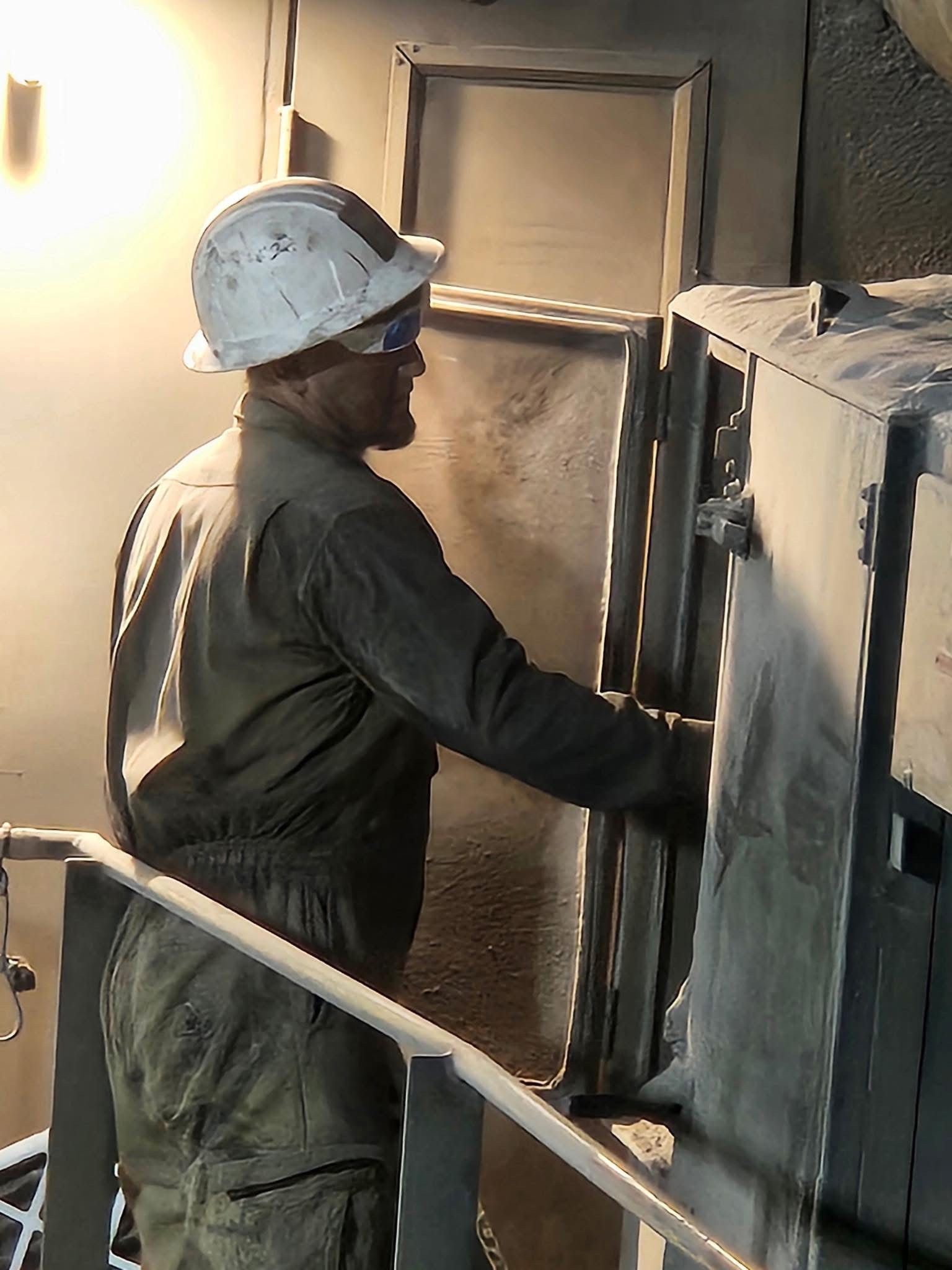 Worker in hard hat opening industrial equipment panel.