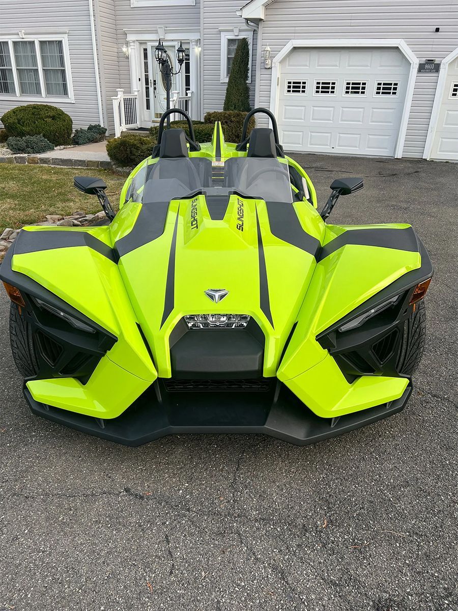A neon yellow slingshot is parked in front of a house.