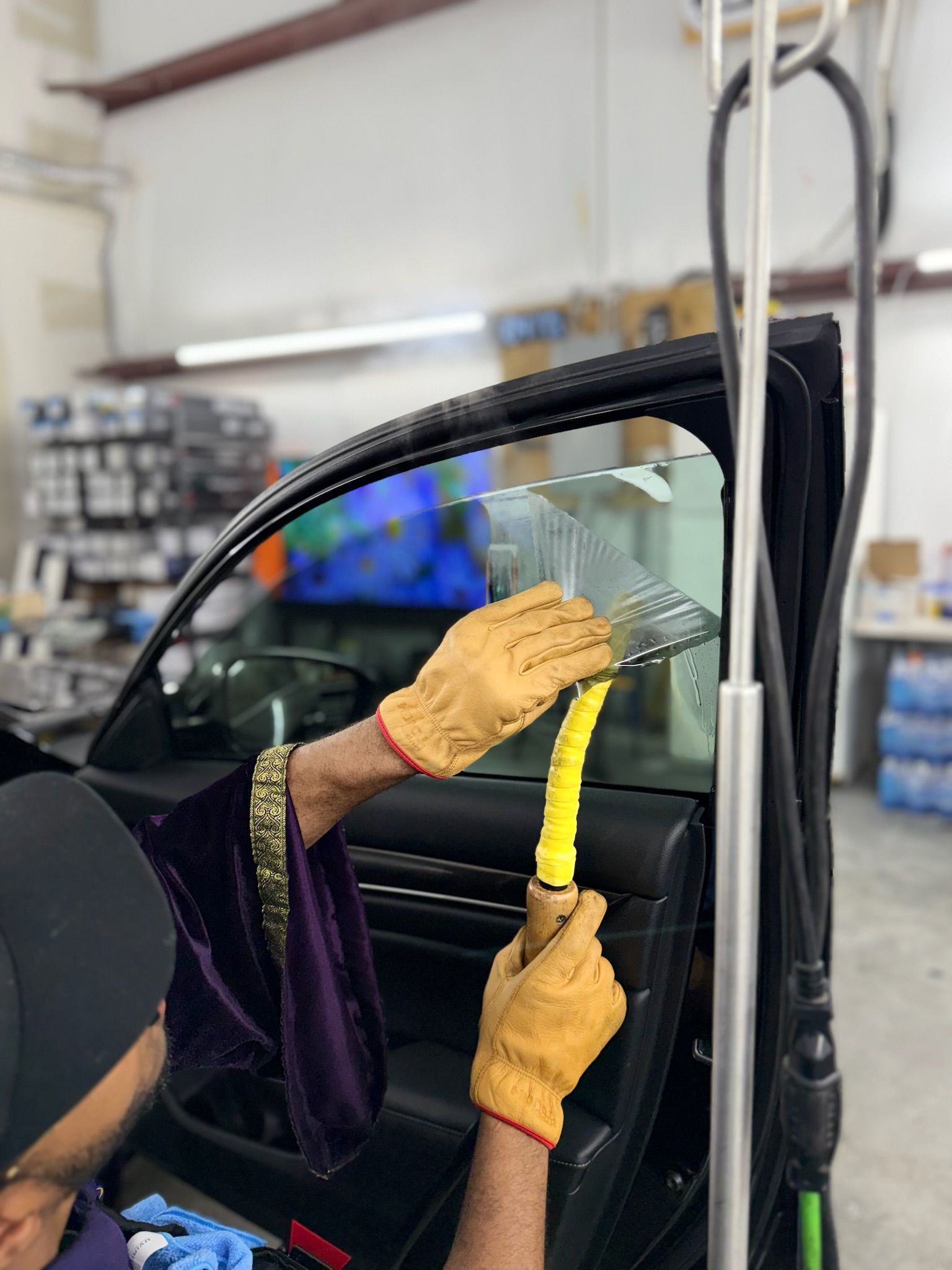 Gloved hands applying yellow protective film to a car windshield in a workshop