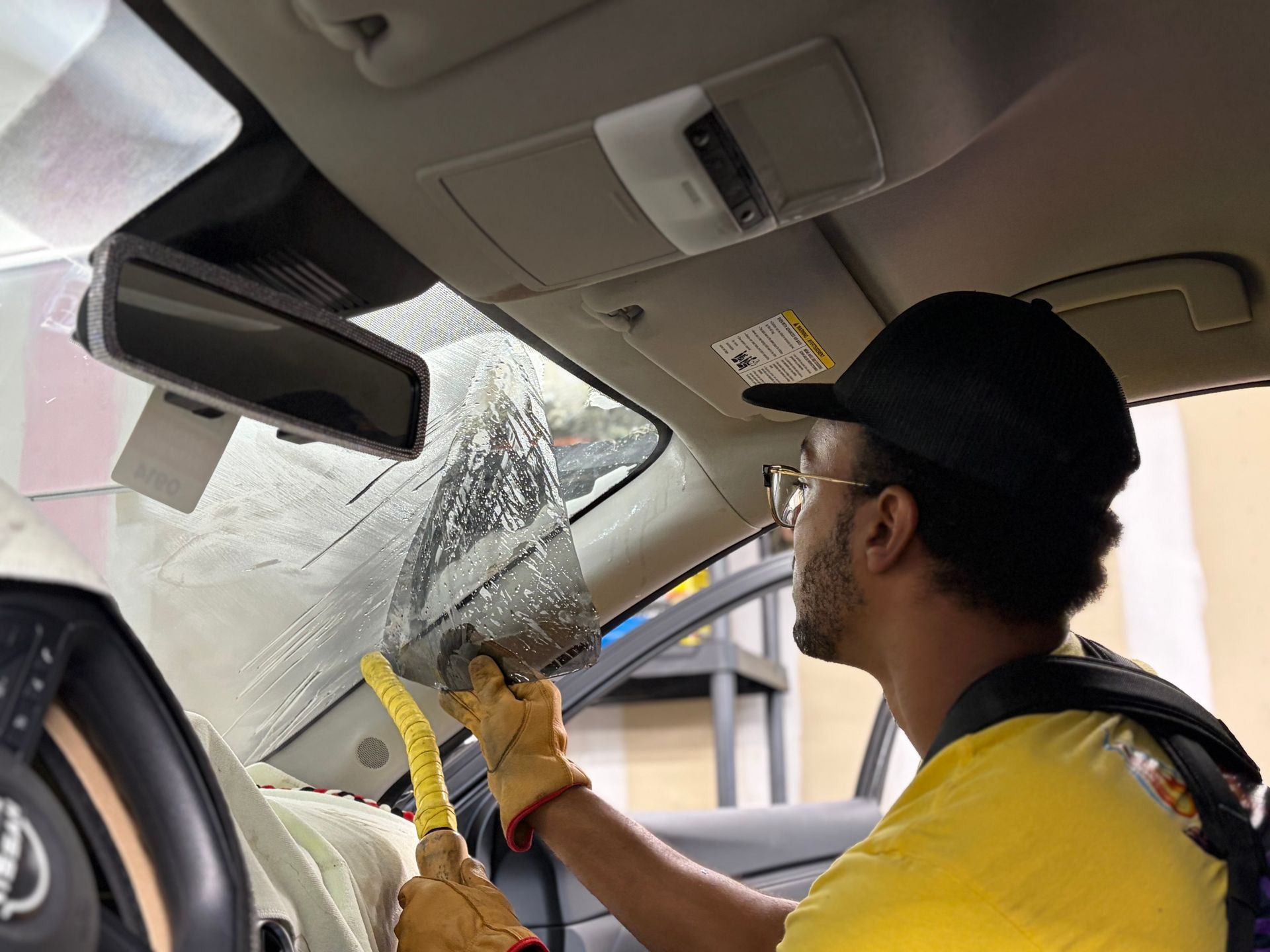 A person using a yellow scraper to remove ice from the inside of a car windshield