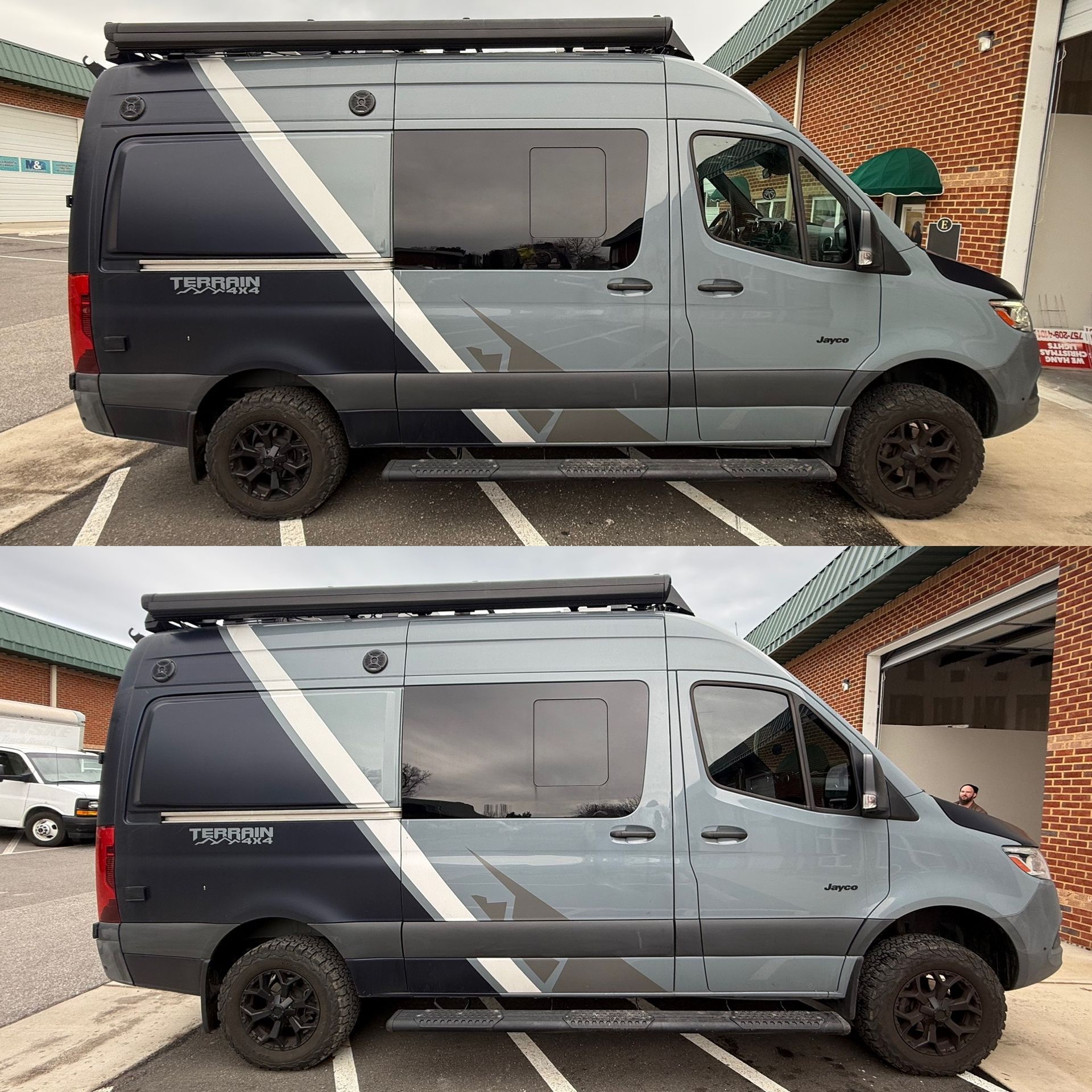 Gray camper van with black roof awning and diagonal stripe, shown in side view parked by a brick house.