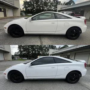 White two-door coupe shown in side view in a driveway, with black wheels and tinted windows.
