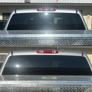 Two silver pickup truck tailgates with dark tinted rear windows and diamond-plate bed covers in a garage