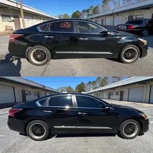 Black sedan with tinted windows parked outside garages, shown in side profile under a bright blue sky.
