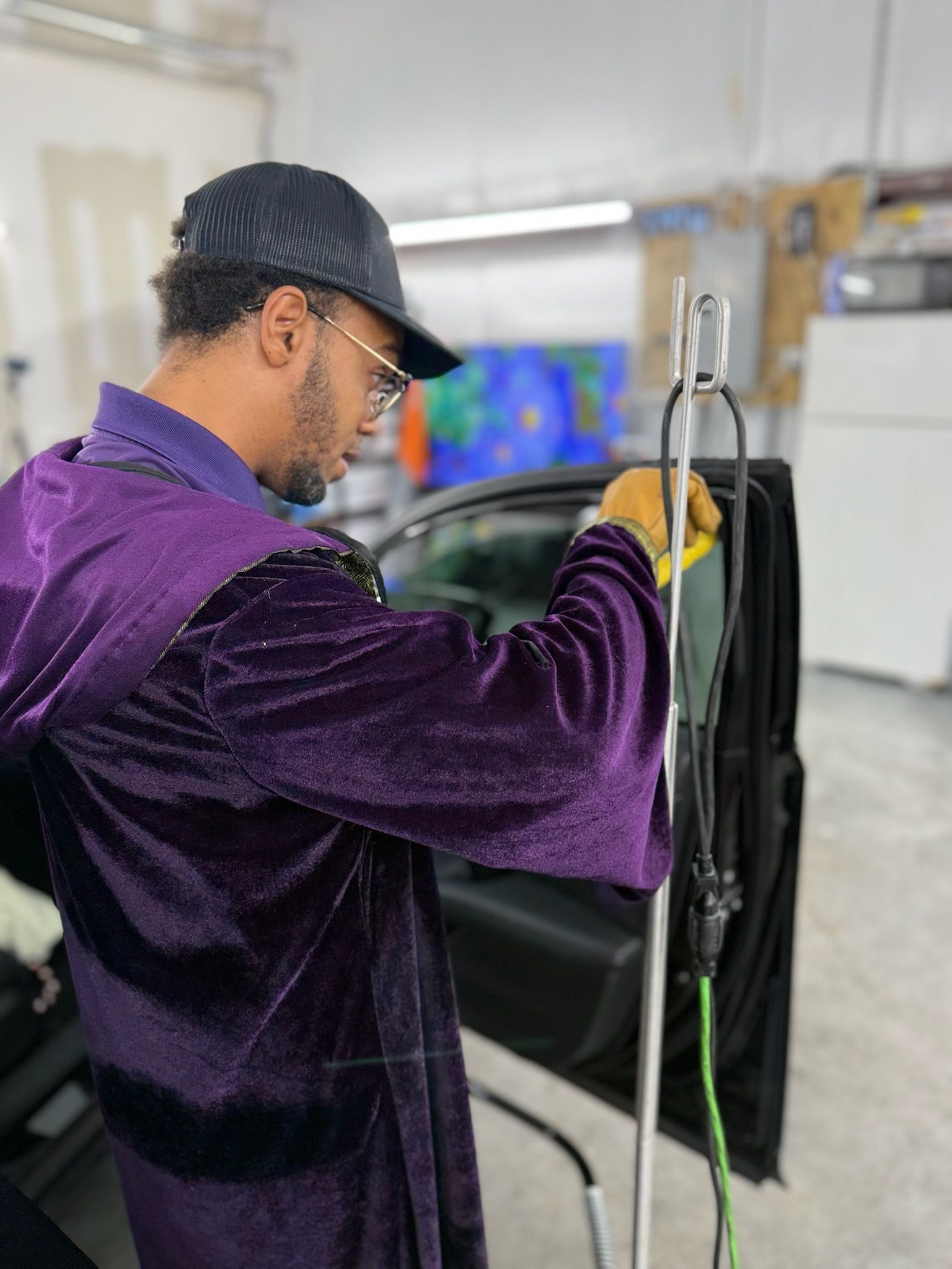 Person in a purple jacket working on a car with a tool in a garage