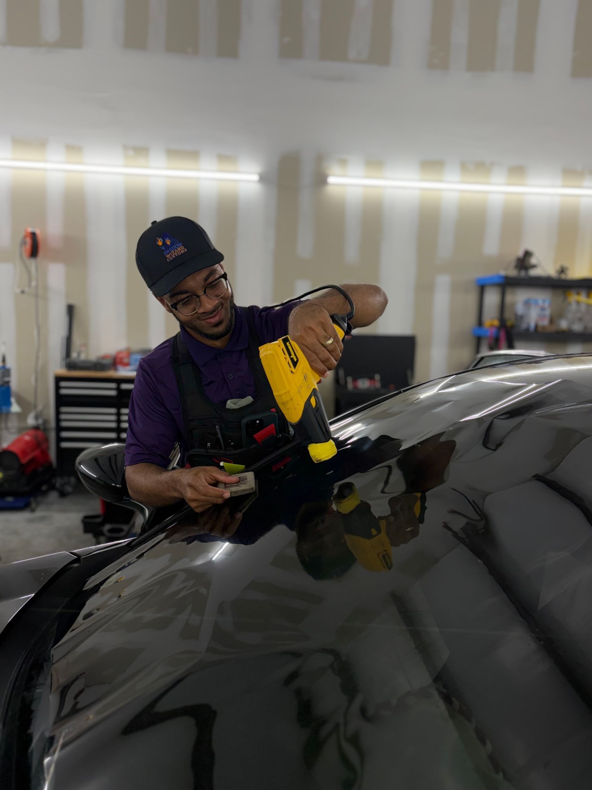 Worker applying yellow film to a car windshield in a workshop