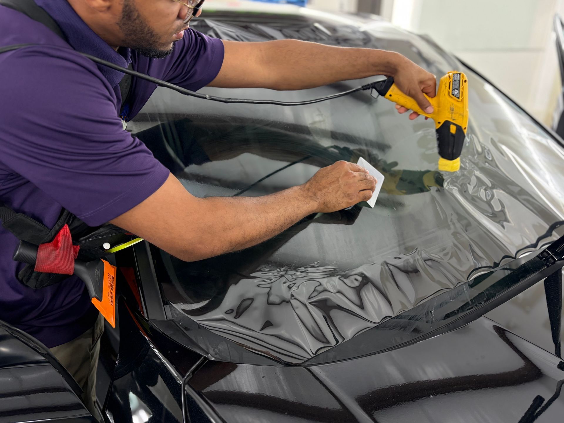 Technician using a drill to repair a car windshield with a black protective cover