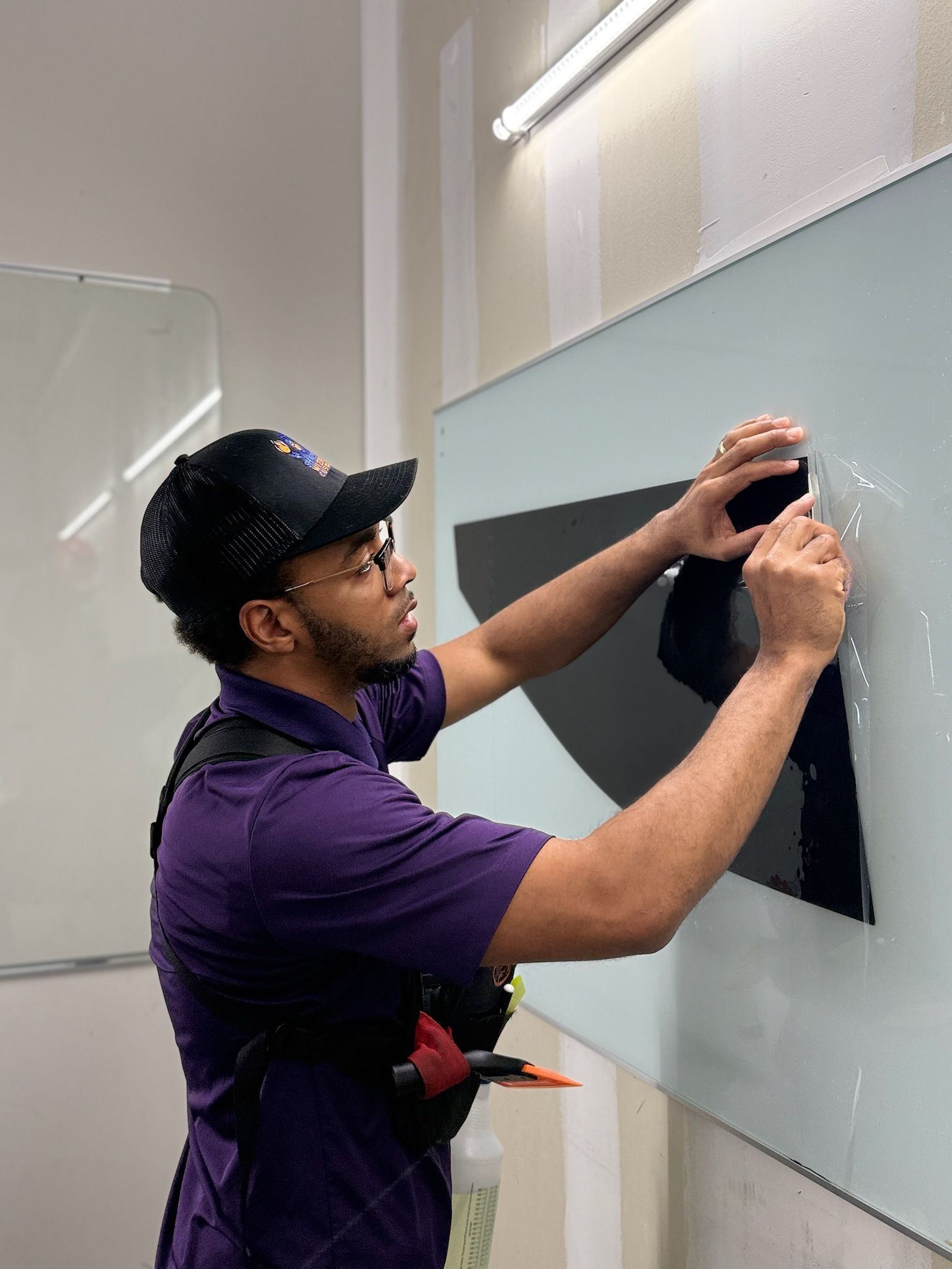 Person hanging a black panel on a wall in a bright indoor room