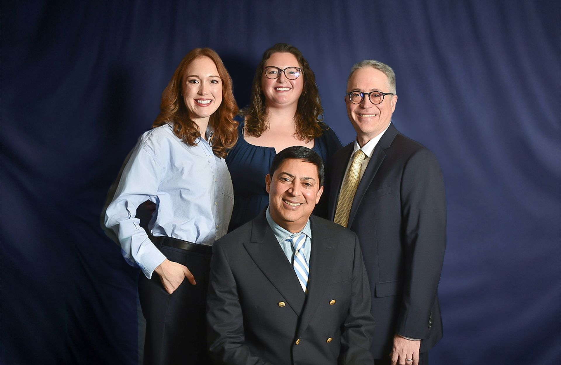 Four people in business attire posing against a dark blue backdrop.