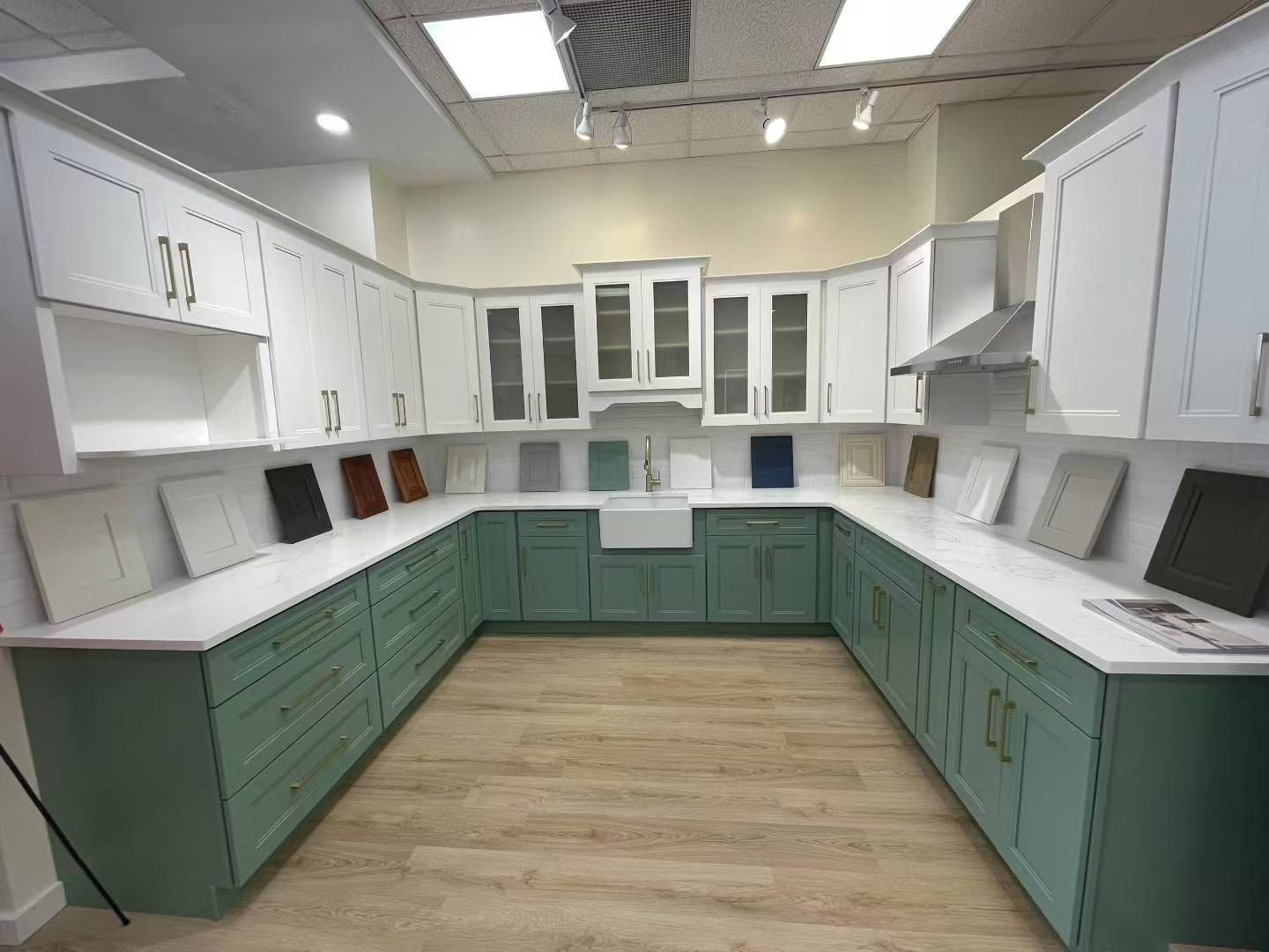 Kitchen display with white upper cabinets, green lower cabinets, and countertop samples.