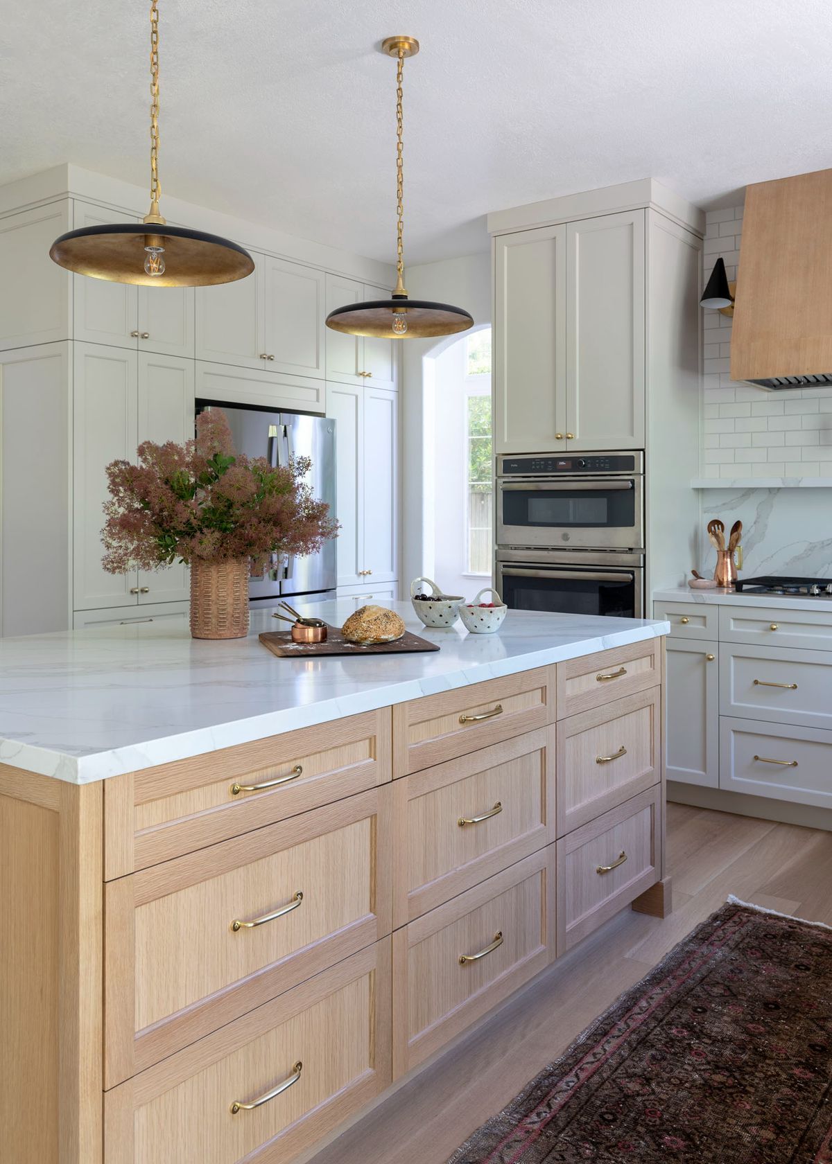 Modern kitchen with light wood cabinetry, white countertops, and gold pendant lights.
